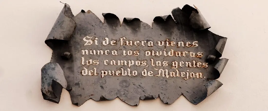 Placa de metal en una fachada con el texto: Si de fuera vienes nunca los olvidarás los campos, las gentes del pueblo de Maleján
